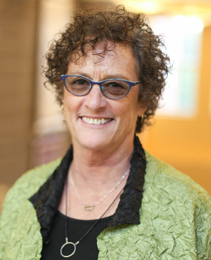 Color headshot of Eileen Ball wearing eyeglasses, necklaces, and green jacket